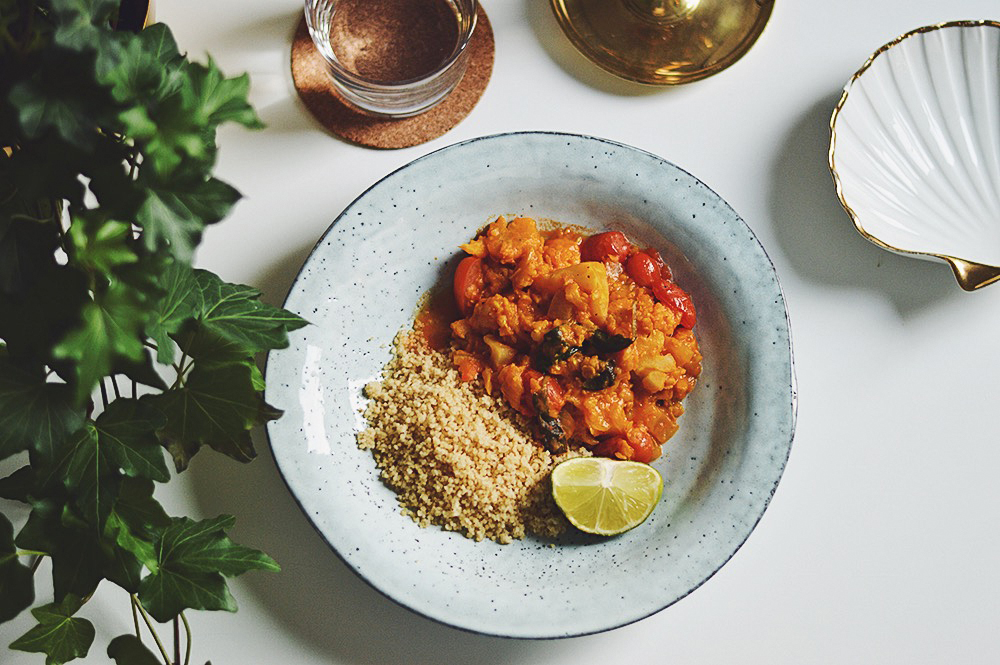 Bilden visar en vegetarisk currygryta med röda linser, kokosmjölk serverat med fluffig couscous, upplagt i en ljusblå tallrik.